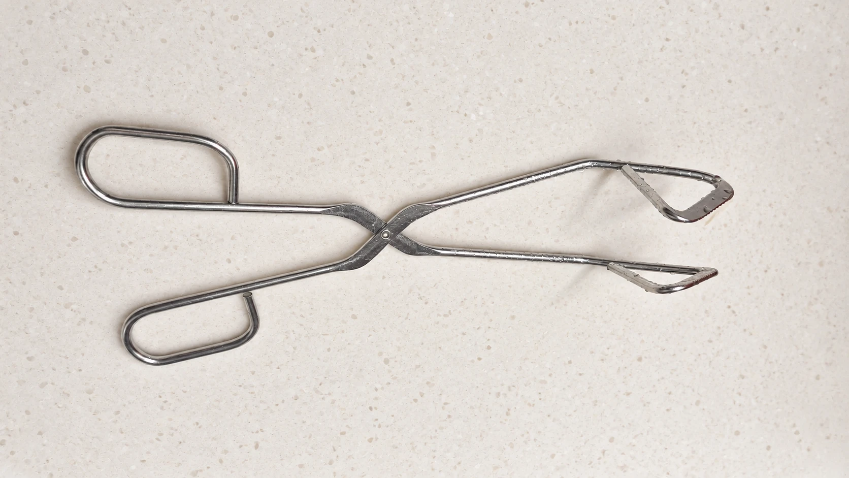 The author’s silver scissor-style kitchen tongs with triangular gripping tips and loop handles on a warm ivory background